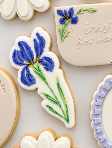 Iris flower-shaped fondant cookie decorated with blue and purple petals, yellow flower detailing and green stems.